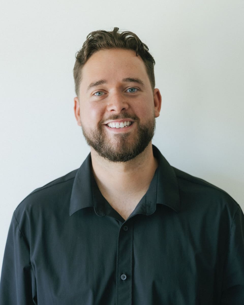Aston Cook, smiling, in a dark shirt against a plain wall.